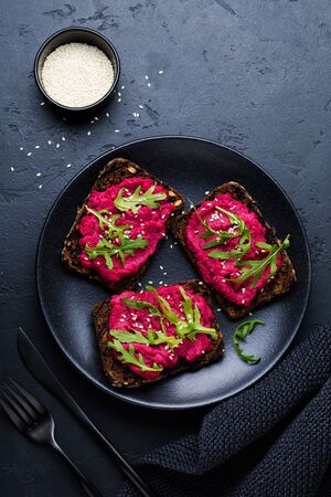 Bruschetta with beetroot hummus, arugula and sesame seeds on dark concrete background. Top view.の写真素材