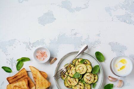 Grilled zucchini salad with basil leaves, yogurt sauce and fried bread in a simple ceramic plate on a white concrete background. Flat lay with copy space.の写真素材