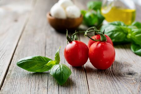 Fresh cherry tomatoes, basil leaves, mozzarella cheese and olive oil on old wooden background.の写真素材