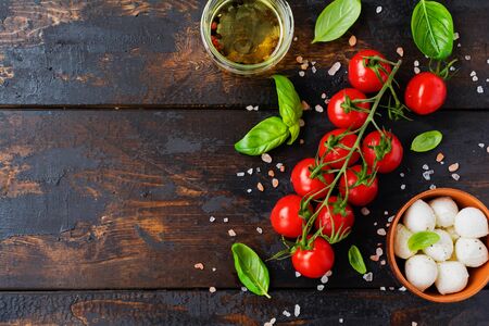 Fresh cherry tomatoes, basil leaves, mozzarella cheese and olive oil on old wooden background. Caprese salad ingredients. Selective focus.の写真素材