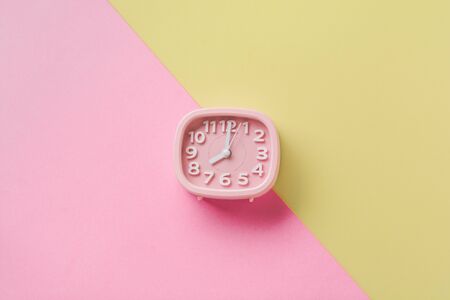 Pink alarm clock lying on yellow surface background. Top view.