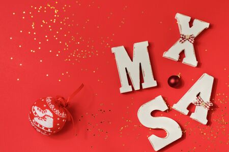 Red ball with a pattern for the Christmas tree, big letters XMAS with gold confetti and toys on a red background. Top view, minimal christmas style and holiday concept. Banner for the site.の写真素材