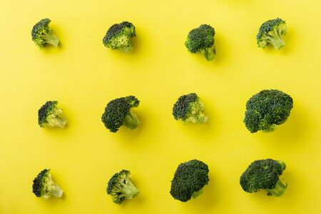 Female hand holds one fresh green broccoli lying on yellow light background. Top view.の写真素材