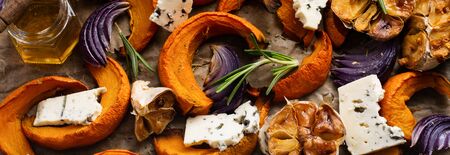 Slices of baked pumpkin, onions, garlic, spices and slices of cheese Dorblu on parchment paper and old blue stone background. Top view.の写真素材