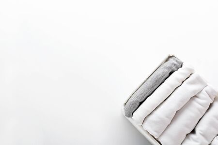 Neatly folded white and gray clothes in a container for a wardrobe or trip on white background....