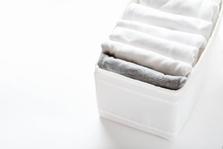 Neatly folded white and gray clothes in a container for a wardrobe or trip on white background....