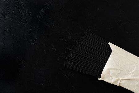 Black spaghetti pasta with cuttlefish ink in a paper bag on a black concrete background. Cooking...
