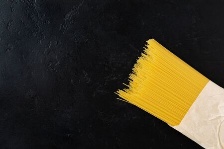 Spaghetti raw pasta in a paper bag on a black concrete background. Cooking concept. Top view with copy space.の写真素材