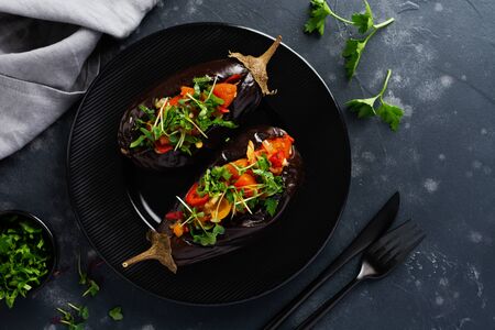 Baked stuffed eggplant with different vegetables, tomato, pepper, onion and parsley on a black stone or concrete table background. Top view.の写真素材