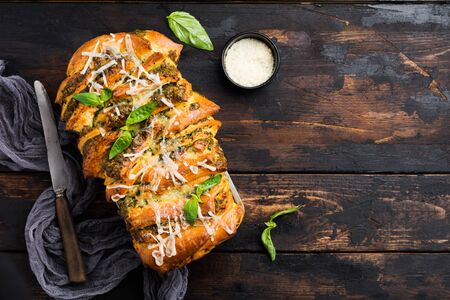 Pull-apart bread with Italian pasta pesto, basil and parmesan cheese in baking form over old dark concrete background. Top view. Rustic stile.の写真素材