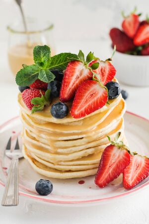 Stack of homemade little pancakes with honey, fresh strawberries and sauce on light wooden background. Selective focus.の写真素材