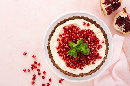 Homemade dessert chocolate tart with coconut cream and pomegranate and mint on a pink table background. Top view.の写真素材