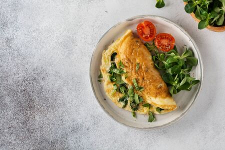 Stuffed omelette with tomatoes, red bell pepper, cream cheese and corn or lamb's lettuce on light concrete background with copy space. Healthy diet food for breakfast. Top view, flat lay.の写真素材