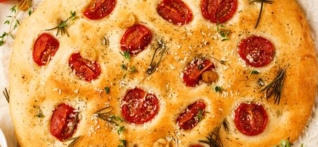 Italian traditional focaccia bread baking with with cherry tomatoes, parmesan and rosemary on light brown background. Top view.の写真素材