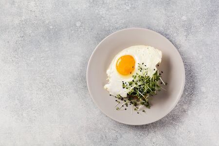 Traditional English breakfast with fried eggs with arugula microgreen in gray ceramic plate on gray concrete old background. Top view.の写真素材