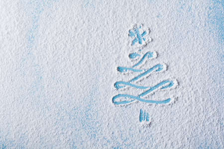 Christmas tree painted on a flour blue background with small toys. View from above.