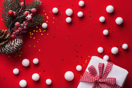 Christmas red background with white snow ornament decoration, fir tree branch and gift box. Flat lay...