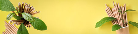 Drinking tubes made of paper and cornstarch, biodegradable material and eco paper glasses with green sprout leaves on yellow trend color 2021 background. Zero waste and plastic free concept. TBanner. Top view.の写真素材
