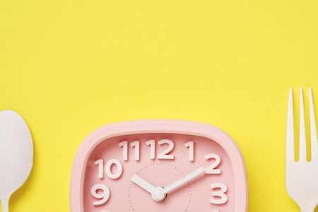 Pink retro alarm clock and white spoon and fork on yellow background with copy space. Time and diet concept.の写真素材