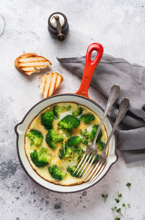 Omelette with broccoli and green young onions on red cast iron pan on old gray concrete background. Top view.の写真素材