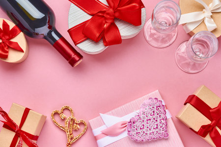 Wine, glasses and gift box in the form of heart with a red ribbon on pink background. Valentines day concept postcard. Top view.の写真素材