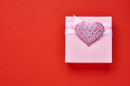Square pink gift box with ribbon and heart on red background. Valentines day concept postcard. Top view.の写真素材