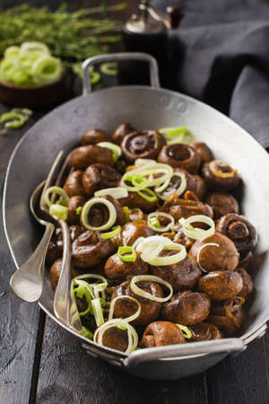 Mushrooms champignon fried in soy sauce, with pepper and steamed onions in an old metal bowl on an old vintage table. Selective focus.の写真素材