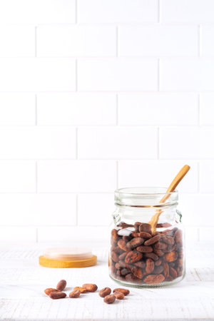 Cocoa beans in a glass jar on a light kitchen table. Culinary food cooking background for making traditional chocolate. Selective focus.の写真素材