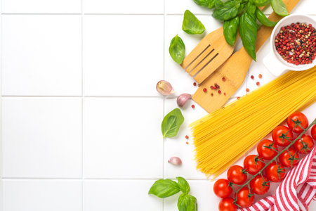 Raw spaghetti with parmesan cheese and tomatoes, basil, garlic and oil on light background with pepper on white table background. Traditional ingredients for preparation of Italian pasta. Top view.の写真素材