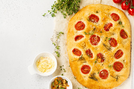 Homemade traditional Italian bread baking with cherry tomatoes, parmesan and rosemary on rustic...
