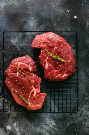 Two Raw beef steak with spices, onions and chili on dark slate or concrete background. Top viewの写真素材