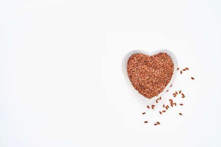 Flax seeds in bowl of the shape of heart isolated on white background, top viewの写真素材