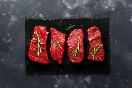 Raw beef steak with spices, onions and rosemary on dark slate or concrete background. Top viewの写真素材