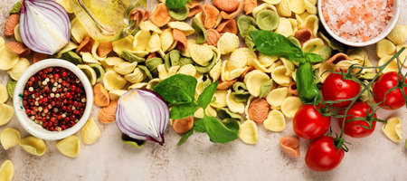 Raw orecchiette with parmesan cheese and tomatoes, basil with garlic and oil on light background. Traditional ingredients for preparation of Italian pasta. Banner. Top view.の写真素材