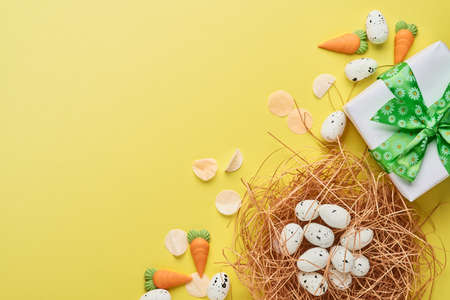 Quail eggs in nest and gift box with green ribbon on yellow trend color background. Easter minimal...
