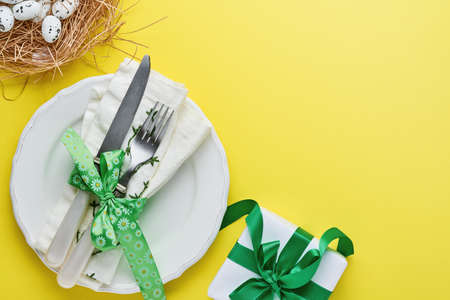 Easter spring greeting table setting with gift box with green ribbon, eggs and sweet carrot on...