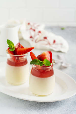 Festive dessert with berry jelly, vanilla panna cota and fresh strawberry on gray concrete table background. Selective focus.の写真素材