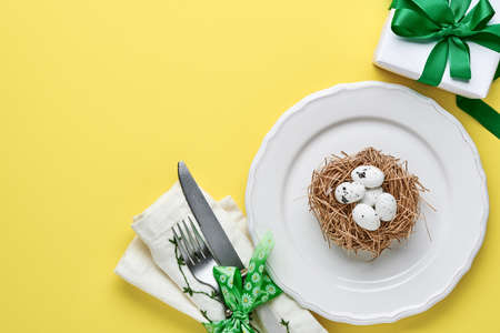 Easter spring greeting table setting with gift box with green ribbon, eggs and sweet carrot on...