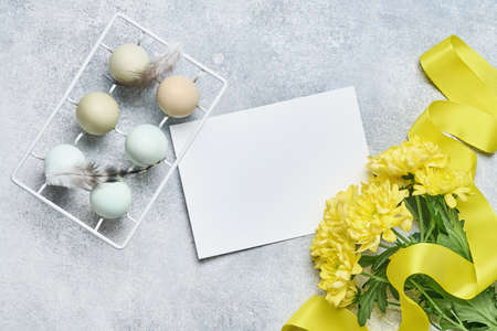 Easter light blue eggs in white vintage metal holder with feathers and yellow chrysanthemums flowers on gray background. Mock up. Spring Happy Easter holiday card.の写真素材