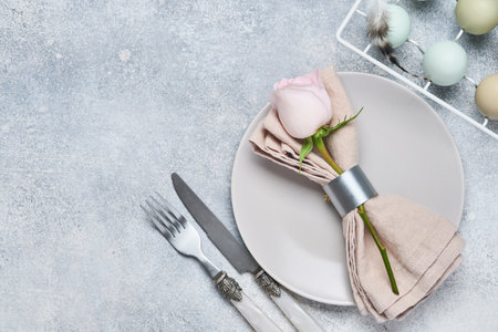 Easter table setting with fresh pink rose on gray stone table. Top view. Elegance Easter holiday...