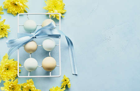 Eggs in white metal holder and flowers on blue background. Mock up. Spring Happy Easter holiday card. Top view.の写真素材