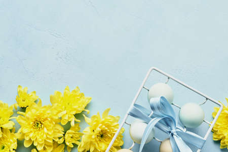 Eggs in white metal holder and flowers on blue background. Mock up. Spring Happy Easter holiday card. Top view.の写真素材