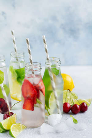 Lots of bottles with refreshing summer lemonade with lime, strawberry, cherry, cucumber and ice on a gray concrete background.の写真素材