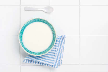 Greek yogurt in blue bowl, linen napkin and wooden spoon on white table. Top view.の写真素材