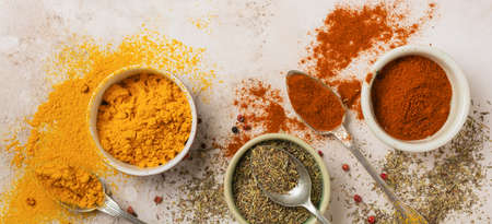 Various spices and seasonings: turmeric, paprika and provencal herbs on light brown stone...