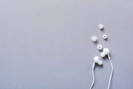 Modern White earphones and mobile phone on a gray background. Minimalist style. Top view with copy...