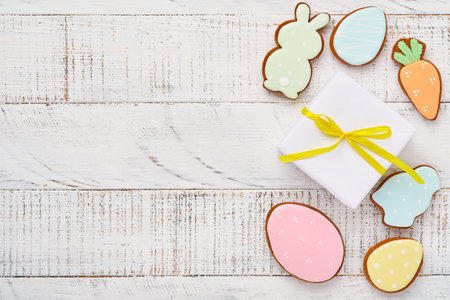 Easter greeting card with colorful rabbits, eggs, chickens and carrots gingerbread cookies on white wooden old background with copy space. Mock up. Banner. Top view.の写真素材