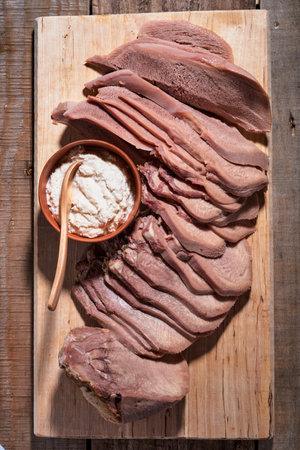 Baked beef tongue sliced, serving with horseradish red and white sauce and meat knife on wooden cutting board over wood background. Top view.の写真素材