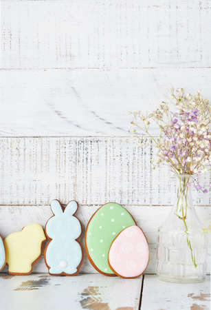 Easter greeting card with colorful rabbits, eggs, chickens and carrots gingerbread cookies on white wooden old background with copy space. Mock up. Banner. Top view.の写真素材