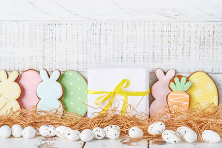 Easter greeting card with colorful rabbits, eggs, chickens and carrots gingerbread cookies on white wooden old background with copy space. Mock up. Banner. Top view.の写真素材